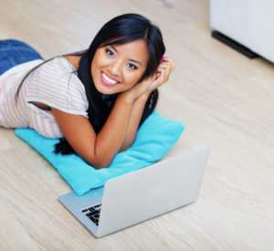 Portrait of young beautiful woman lying on clean floor with laptop at home