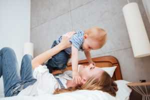 Happy young mother playing and having fun with her little son on bed at home